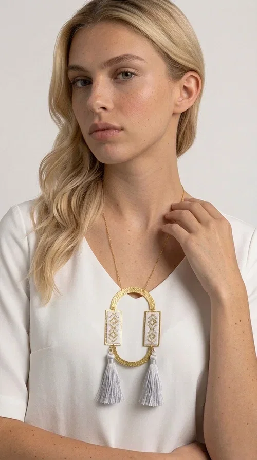 , An embroidered necklace that combines tradition with contemporary design — the Statement Necklace KOL-4757 is the ideal choice for every woman who wants to express herself through her jewelry. Designed by Greek Jewelry Designer Aikaterini Chalkiadaki, this handmade necklace is a unique combination of fabric and brass, inspired by folk art and the geometric motifs of Greek tradition.

Two embroidered rectangular plates with geometric patterns in white and gold frame a hammered gold brass circle, while three light-colored tassels add movement and character. The long gold chain completes a composition that is both statement-making and harmonious. Ideal for summer looks, casual outfits, and evening moments when you want to stand out.