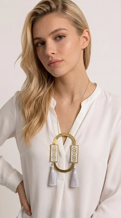 , An embroidered necklace that combines tradition with contemporary design — the Statement Necklace KOL-4757 is the ideal choice for every woman who wants to express herself through her jewelry. Designed by Greek Jewelry Designer Aikaterini Chalkiadaki, this handmade necklace is a unique combination of fabric and brass, inspired by folk art and the geometric motifs of Greek tradition.

Two embroidered rectangular plates with geometric patterns in white and gold frame a hammered gold brass circle, while three light-colored tassels add movement and character. The long gold chain completes a composition that is both statement-making and harmonious. Ideal for summer looks, casual outfits, and evening moments when you want to stand out.