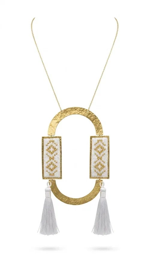 , An embroidered necklace that combines tradition with contemporary design — the Statement Necklace KOL-4757 is the ideal choice for every woman who wants to express herself through her jewelry. Designed by Greek Jewelry Designer Aikaterini Chalkiadaki, this handmade necklace is a unique combination of fabric and brass, inspired by folk art and the geometric motifs of Greek tradition.

Two embroidered rectangular plates with geometric patterns in white and gold frame a hammered gold brass circle, while three light-colored tassels add movement and character. The long gold chain completes a composition that is both statement-making and harmonious. Ideal for summer looks, casual outfits, and evening moments when you want to stand out.