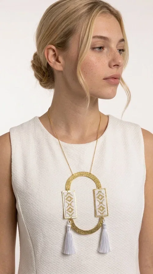 , An embroidered necklace that combines tradition with contemporary design — the Statement Necklace KOL-4757 is the ideal choice for every woman who wants to express herself through her jewelry. Designed by Greek Jewelry Designer Aikaterini Chalkiadaki, this handmade necklace is a unique combination of fabric and brass, inspired by folk art and the geometric motifs of Greek tradition.

Two embroidered rectangular plates with geometric patterns in white and gold frame a hammered gold brass circle, while three light-colored tassels add movement and character. The long gold chain completes a composition that is both statement-making and harmonious. Ideal for summer looks, casual outfits, and evening moments when you want to stand out.