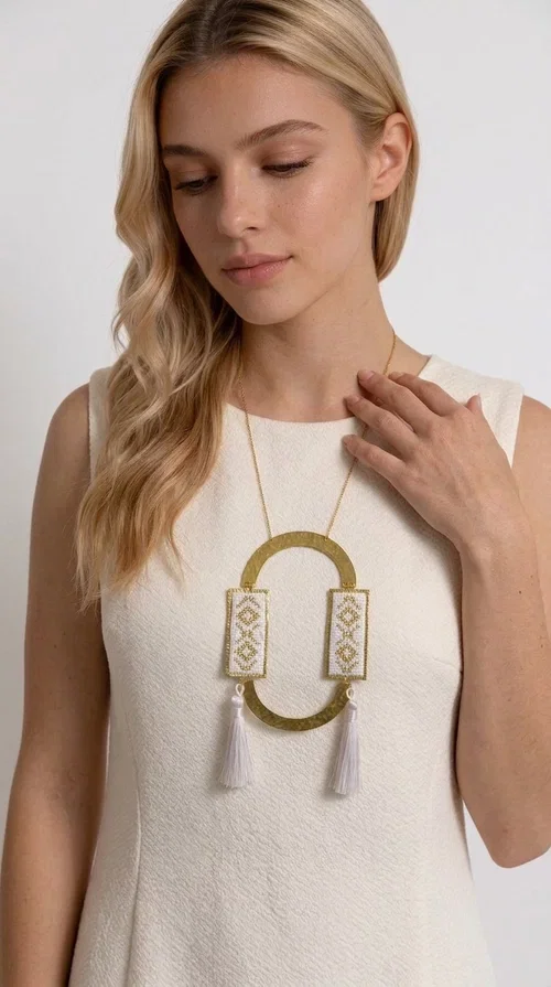 , An embroidered necklace that combines tradition with contemporary design — the Statement Necklace KOL-4757 is the ideal choice for every woman who wants to express herself through her jewelry. Designed by Greek Jewelry Designer Aikaterini Chalkiadaki, this handmade necklace is a unique combination of fabric and brass, inspired by folk art and the geometric motifs of Greek tradition.

Two embroidered rectangular plates with geometric patterns in white and gold frame a hammered gold brass circle, while three light-colored tassels add movement and character. The long gold chain completes a composition that is both statement-making and harmonious. Ideal for summer looks, casual outfits, and evening moments when you want to stand out.