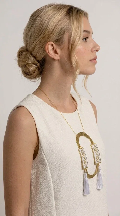 , An embroidered necklace that combines tradition with contemporary design — the Statement Necklace KOL-4757 is the ideal choice for every woman who wants to express herself through her jewelry. Designed by Greek Jewelry Designer Aikaterini Chalkiadaki, this handmade necklace is a unique combination of fabric and brass, inspired by folk art and the geometric motifs of Greek tradition.

Two embroidered rectangular plates with geometric patterns in white and gold frame a hammered gold brass circle, while three light-colored tassels add movement and character. The long gold chain completes a composition that is both statement-making and harmonious. Ideal for summer looks, casual outfits, and evening moments when you want to stand out.