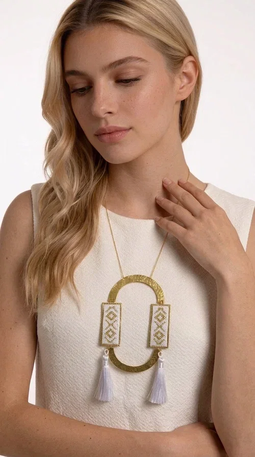 , An embroidered necklace that combines tradition with contemporary design — the Statement Necklace KOL-4757 is the ideal choice for every woman who wants to express herself through her jewelry. Designed by Greek Jewelry Designer Aikaterini Chalkiadaki, this handmade necklace is a unique combination of fabric and brass, inspired by folk art and the geometric motifs of Greek tradition.

Two embroidered rectangular plates with geometric patterns in white and gold frame a hammered gold brass circle, while three light-colored tassels add movement and character. The long gold chain completes a composition that is both statement-making and harmonious. Ideal for summer looks, casual outfits, and evening moments when you want to stand out.
