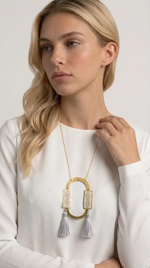 , An embroidered necklace that combines tradition with contemporary design — the Statement Necklace KOL-4757 is the ideal choice for every woman who wants to express herself through her jewelry. Designed by Greek Jewelry Designer Aikaterini Chalkiadaki, this handmade necklace is a unique combination of fabric and brass, inspired by folk art and the geometric motifs of Greek tradition.

Two embroidered rectangular plates with geometric patterns in white and gold frame a hammered gold brass circle, while three light-colored tassels add movement and character. The long gold chain completes a composition that is both statement-making and harmonious. Ideal for summer looks, casual outfits, and evening moments when you want to stand out.