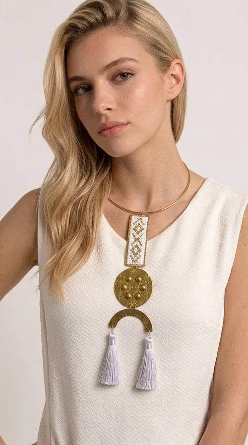 , A statement embroidered necklace that doesn't go unnoticed — featuring geometric patterns inspired by Greek tradition and an aesthetic that blends folk with contemporary style.

Designed by Greek Jewelry Designer Aikaterini Chalkiadaki, this handmade necklace consists of an embroidered rectangular section in white and gold with diamond-shaped geometric motifs, a round brass pendant with embossed details, and a semi-circular element from which two elegant white tassels hang. The piece is worn on a delicate gold torque-style chain that sits comfortably around the neck.

Ideal for those seeking striking jewelry that tells a story, this long necklace pairs equally well with a simple white shirt, a summer dress, or a boho outfit. Its white-and-gold palette makes it versatile for both day and evening wear.
