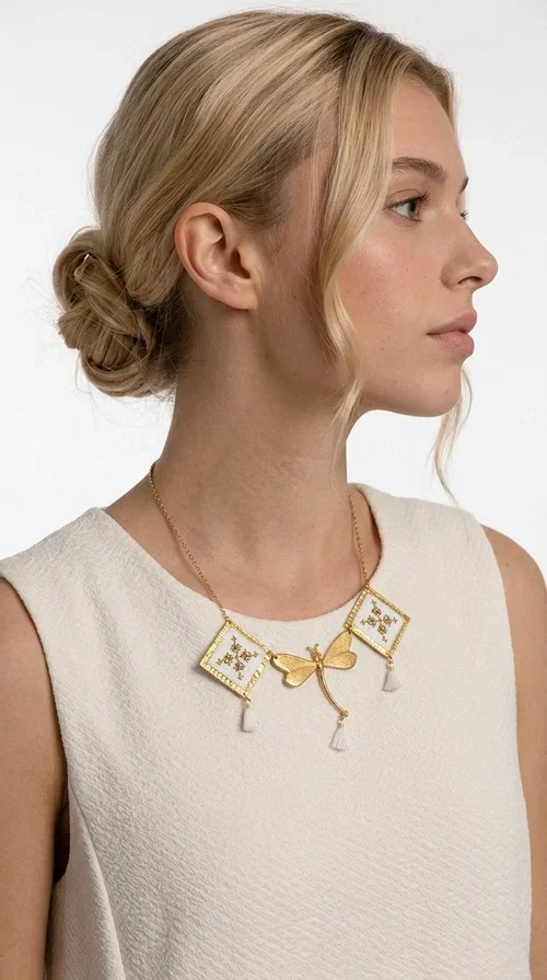 , The statement embroidered necklace in white with geometric patterns is a piece of jewelry that combines the traditional art of embroidery with a modern, striking result. Designed by Greek Jewelry Designer Aikaterini Chalkiadaki, this unique necklace showcases Greek craftsmanship in all its glory.

The necklace features two embroidered square elements in white with gold geometric motifs inspired by Greek folk tradition, joined by a gold dragonfly-shaped element. Three delicate white tassels add movement and joy to the piece, while the gold chain completes the look with elegance. The contrast between the white fabric and the brass creates a result that is both delicate and striking.

Ideal for summer looks, brunch, weddings, or evening outings, this handmade necklace pairs equally well with a simple white T-shirt or a boho dress. It also makes an excellent gift choice for women who love unique, handmade jewelry.