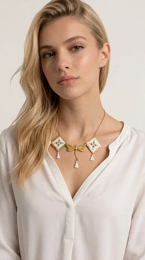 , The statement embroidered necklace in white with geometric patterns is a piece of jewelry that combines the traditional art of embroidery with a modern, striking result. Designed by Greek Jewelry Designer Aikaterini Chalkiadaki, this unique necklace showcases Greek craftsmanship in all its glory.

The necklace features two embroidered square elements in white with gold geometric motifs inspired by Greek folk tradition, joined by a gold dragonfly-shaped element. Three delicate white tassels add movement and joy to the piece, while the gold chain completes the look with elegance. The contrast between the white fabric and the brass creates a result that is both delicate and striking.

Ideal for summer looks, brunch, weddings, or evening outings, this handmade necklace pairs equally well with a simple white T-shirt or a boho dress. It also makes an excellent gift choice for women who love unique, handmade jewelry.