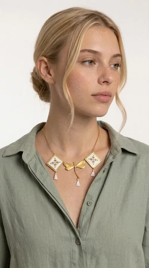 , The statement embroidered necklace in white with geometric patterns is a piece of jewelry that combines the traditional art of embroidery with a modern, striking result. Designed by Greek Jewelry Designer Aikaterini Chalkiadaki, this unique necklace showcases Greek craftsmanship in all its glory.

The necklace features two embroidered square elements in white with gold geometric motifs inspired by Greek folk tradition, joined by a gold dragonfly-shaped element. Three delicate white tassels add movement and joy to the piece, while the gold chain completes the look with elegance. The contrast between the white fabric and the brass creates a result that is both delicate and striking.

Ideal for summer looks, brunch, weddings, or evening outings, this handmade necklace pairs equally well with a simple white T-shirt or a boho dress. It also makes an excellent gift choice for women who love unique, handmade jewelry.