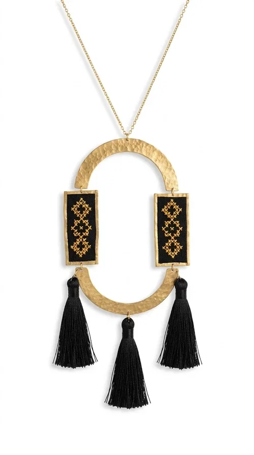 , A statement embroidered necklace that blends tradition with modern aesthetics — ideal for every woman who wants to express herself with style and character.

Designed by Greek Jewelry Designer Aikaterini Chalkiadaki, this striking long necklace is an ode to folk art and craftsmanship. Two rectangular embroidered plaques with geometric patterns in black and gold are framed by a golden brass arch, while three black tassels add movement and boho-chic charm. The gold-tone chain completes the composition with an elegant finishing touch.

This embroidered necklace pairs beautifully with simple white or ecru outfits that let the piece take center stage, as well as with evening looks that need that extra touch. Worn alone, it instantly turns any look into a statement.