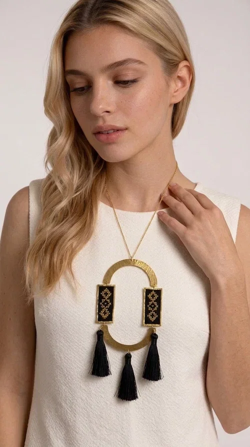 , A statement embroidered necklace that blends tradition with modern aesthetics — ideal for every woman who wants to express herself with style and character.

Designed by Greek Jewelry Designer Aikaterini Chalkiadaki, this striking long necklace is an ode to folk art and craftsmanship. Two rectangular embroidered plaques with geometric patterns in black and gold are framed by a golden brass arch, while three black tassels add movement and boho-chic charm. The gold-tone chain completes the composition with an elegant finishing touch.

This embroidered necklace pairs beautifully with simple white or ecru outfits that let the piece take center stage, as well as with evening looks that need that extra touch. Worn alone, it instantly turns any look into a statement.