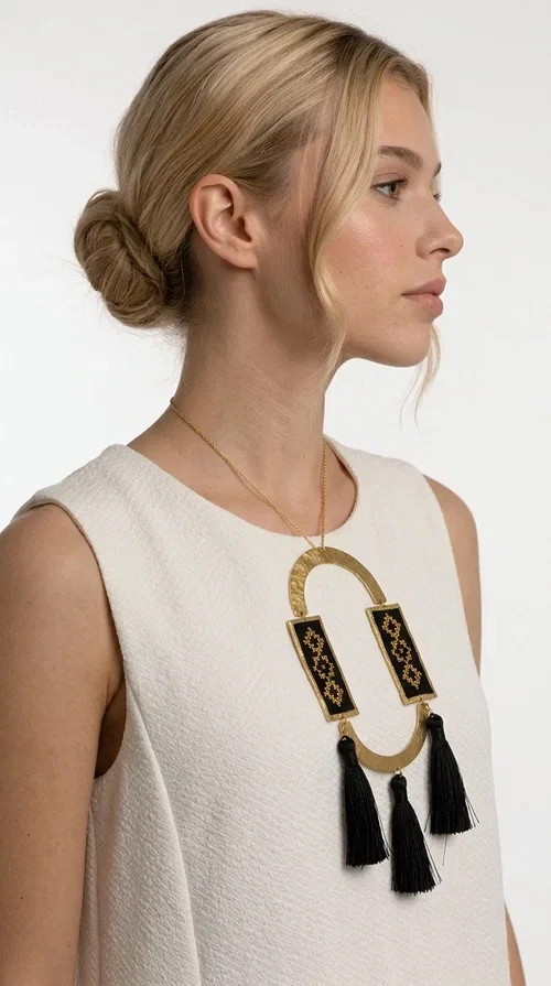 , A statement embroidered necklace that blends tradition with modern aesthetics — ideal for every woman who wants to express herself with style and character.

Designed by Greek Jewelry Designer Aikaterini Chalkiadaki, this striking long necklace is an ode to folk art and craftsmanship. Two rectangular embroidered plaques with geometric patterns in black and gold are framed by a golden brass arch, while three black tassels add movement and boho-chic charm. The gold-tone chain completes the composition with an elegant finishing touch.

This embroidered necklace pairs beautifully with simple white or ecru outfits that let the piece take center stage, as well as with evening looks that need that extra touch. Worn alone, it instantly turns any look into a statement.