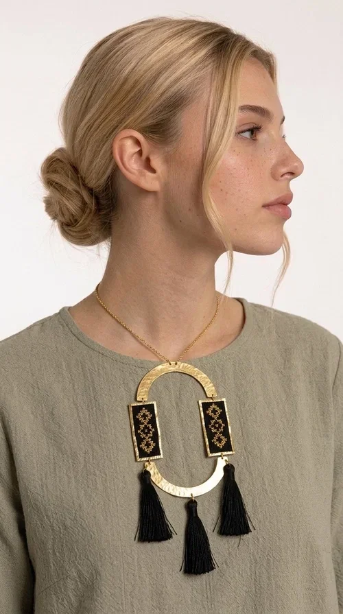 , A statement embroidered necklace that blends tradition with modern aesthetics — ideal for every woman who wants to express herself with style and character.

Designed by Greek Jewelry Designer Aikaterini Chalkiadaki, this striking long necklace is an ode to folk art and craftsmanship. Two rectangular embroidered plaques with geometric patterns in black and gold are framed by a golden brass arch, while three black tassels add movement and boho-chic charm. The gold-tone chain completes the composition with an elegant finishing touch.

This embroidered necklace pairs beautifully with simple white or ecru outfits that let the piece take center stage, as well as with evening looks that need that extra touch. Worn alone, it instantly turns any look into a statement.