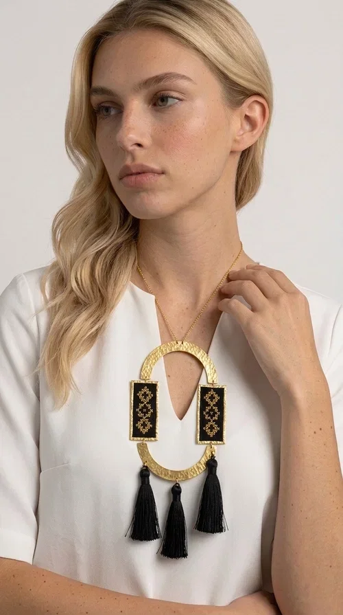 , A statement embroidered necklace that blends tradition with modern aesthetics — ideal for every woman who wants to express herself with style and character.

Designed by Greek Jewelry Designer Aikaterini Chalkiadaki, this striking long necklace is an ode to folk art and craftsmanship. Two rectangular embroidered plaques with geometric patterns in black and gold are framed by a golden brass arch, while three black tassels add movement and boho-chic charm. The gold-tone chain completes the composition with an elegant finishing touch.

This embroidered necklace pairs beautifully with simple white or ecru outfits that let the piece take center stage, as well as with evening looks that need that extra touch. Worn alone, it instantly turns any look into a statement.