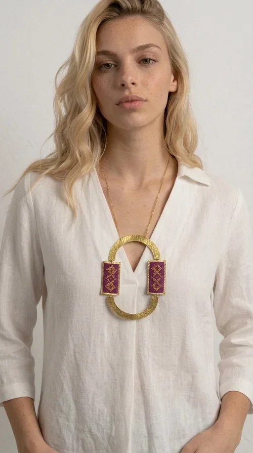 , An embroidered necklace that instantly catches the eye — the Statement Necklace KOL-4753 combines the tradition of Greek embroidery art with a modern, geometric aesthetic. Designed by Greek Jewelry Designer Aikaterini Chalkiadaki, this striking long necklace is the ultimate statement piece for every woman who appreciates handmade artistry and uniqueness.

The necklace features two rectangular fabric elements in deep burgundy, adorned with gold embroidery of geometric patterns inspired by folklore aesthetics. The embroidered sections are framed by shiny gold-toned brass, forming a large oval shape — a bold design choice that highlights the uniqueness of the piece. The gold-toned chain offers an elegant long line that pairs perfectly with simple, monochrome outfits.

Ideal for stylish daytime looks as well as evening outings, this necklace suits both casual and formal ensembles equally well. It gives your look an authentic, artistic character.
