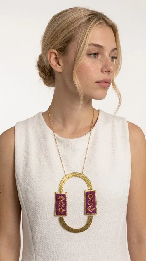 , An embroidered necklace that instantly catches the eye — the Statement Necklace KOL-4753 combines the tradition of Greek embroidery art with a modern, geometric aesthetic. Designed by Greek Jewelry Designer Aikaterini Chalkiadaki, this striking long necklace is the ultimate statement piece for every woman who appreciates handmade artistry and uniqueness.

The necklace features two rectangular fabric elements in deep burgundy, adorned with gold embroidery of geometric patterns inspired by folklore aesthetics. The embroidered sections are framed by shiny gold-toned brass, forming a large oval shape — a bold design choice that highlights the uniqueness of the piece. The gold-toned chain offers an elegant long line that pairs perfectly with simple, monochrome outfits.

Ideal for stylish daytime looks as well as evening outings, this necklace suits both casual and formal ensembles equally well. It gives your look an authentic, artistic character.