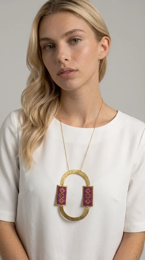 , An embroidered necklace that instantly catches the eye — the Statement Necklace KOL-4753 combines the tradition of Greek embroidery art with a modern, geometric aesthetic. Designed by Greek Jewelry Designer Aikaterini Chalkiadaki, this striking long necklace is the ultimate statement piece for every woman who appreciates handmade artistry and uniqueness.

The necklace features two rectangular fabric elements in deep burgundy, adorned with gold embroidery of geometric patterns inspired by folklore aesthetics. The embroidered sections are framed by shiny gold-toned brass, forming a large oval shape — a bold design choice that highlights the uniqueness of the piece. The gold-toned chain offers an elegant long line that pairs perfectly with simple, monochrome outfits.

Ideal for stylish daytime looks as well as evening outings, this necklace suits both casual and formal ensembles equally well. It gives your look an authentic, artistic character.
