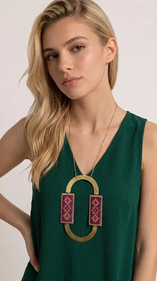 , An embroidered necklace that instantly catches the eye — the Statement Necklace KOL-4753 combines the tradition of Greek embroidery art with a modern, geometric aesthetic. Designed by Greek Jewelry Designer Aikaterini Chalkiadaki, this striking long necklace is the ultimate statement piece for every woman who appreciates handmade artistry and uniqueness.

The necklace features two rectangular fabric elements in deep burgundy, adorned with gold embroidery of geometric patterns inspired by folklore aesthetics. The embroidered sections are framed by shiny gold-toned brass, forming a large oval shape — a bold design choice that highlights the uniqueness of the piece. The gold-toned chain offers an elegant long line that pairs perfectly with simple, monochrome outfits.

Ideal for stylish daytime looks as well as evening outings, this necklace suits both casual and formal ensembles equally well. It gives your look an authentic, artistic character.
