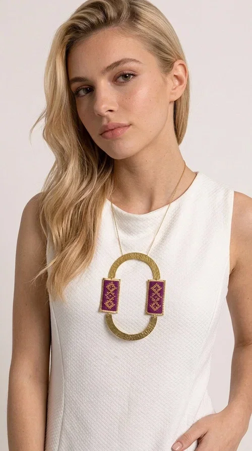 , An embroidered necklace that instantly catches the eye — the Statement Necklace KOL-4753 combines the tradition of Greek embroidery art with a modern, geometric aesthetic. Designed by Greek Jewelry Designer Aikaterini Chalkiadaki, this striking long necklace is the ultimate statement piece for every woman who appreciates handmade artistry and uniqueness.

The necklace features two rectangular fabric elements in deep burgundy, adorned with gold embroidery of geometric patterns inspired by folklore aesthetics. The embroidered sections are framed by shiny gold-toned brass, forming a large oval shape — a bold design choice that highlights the uniqueness of the piece. The gold-toned chain offers an elegant long line that pairs perfectly with simple, monochrome outfits.

Ideal for stylish daytime looks as well as evening outings, this necklace suits both casual and formal ensembles equally well. It gives your look an authentic, artistic character.
