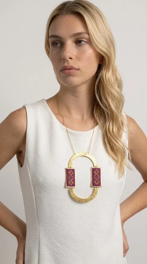 , An embroidered necklace that instantly catches the eye — the Statement Necklace KOL-4753 combines the tradition of Greek embroidery art with a modern, geometric aesthetic. Designed by Greek Jewelry Designer Aikaterini Chalkiadaki, this striking long necklace is the ultimate statement piece for every woman who appreciates handmade artistry and uniqueness.

The necklace features two rectangular fabric elements in deep burgundy, adorned with gold embroidery of geometric patterns inspired by folklore aesthetics. The embroidered sections are framed by shiny gold-toned brass, forming a large oval shape — a bold design choice that highlights the uniqueness of the piece. The gold-toned chain offers an elegant long line that pairs perfectly with simple, monochrome outfits.

Ideal for stylish daytime looks as well as evening outings, this necklace suits both casual and formal ensembles equally well. It gives your look an authentic, artistic character.
