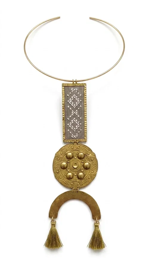 , The ecru embroidered statement necklace with geometric patterns is a piece of jewelry that combines the traditional art of embroidery with modern aesthetics, creating an immediately eye-catching result. Designed by Greek jewelry designer Aikaterini Chalkiadaki, this handmade necklace is a distinctive choice for women who appreciate uniqueness and authentic craftsmanship.

The necklace features a rectangular embroidered section with fine geometric motifs in an ecru shade, paired with a circular brass element featuring embossed details and a semicircular arch. Three dangling khaki-olive tassels add movement and a boho-folklore character, while the base of the necklace consists of a semi-rigid metallic neckwire that rests comfortably on the collarbone. The combination of brass and fabric makes it lightweight to wear, despite its striking appearance.

Ideal for summer outfits, boho looks, ethnic, and festival styles, it pairs perfectly with linen shirts, maxi dresses, or simple tops. It is also an excellent gift idea for women who love large, statement jewelry.