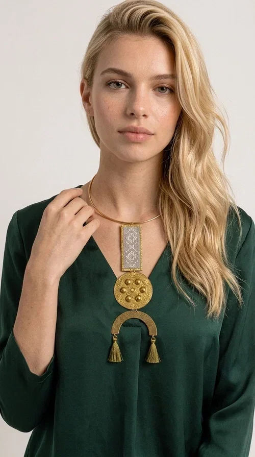 , The ecru embroidered statement necklace with geometric patterns is a piece of jewelry that combines the traditional art of embroidery with modern aesthetics, creating an immediately eye-catching result. Designed by Greek jewelry designer Aikaterini Chalkiadaki, this handmade necklace is a distinctive choice for women who appreciate uniqueness and authentic craftsmanship.

The necklace features a rectangular embroidered section with fine geometric motifs in an ecru shade, paired with a circular brass element featuring embossed details and a semicircular arch. Three dangling khaki-olive tassels add movement and a boho-folklore character, while the base of the necklace consists of a semi-rigid metallic neckwire that rests comfortably on the collarbone. The combination of brass and fabric makes it lightweight to wear, despite its striking appearance.

Ideal for summer outfits, boho looks, ethnic, and festival styles, it pairs perfectly with linen shirts, maxi dresses, or simple tops. It is also an excellent gift idea for women who love large, statement jewelry.