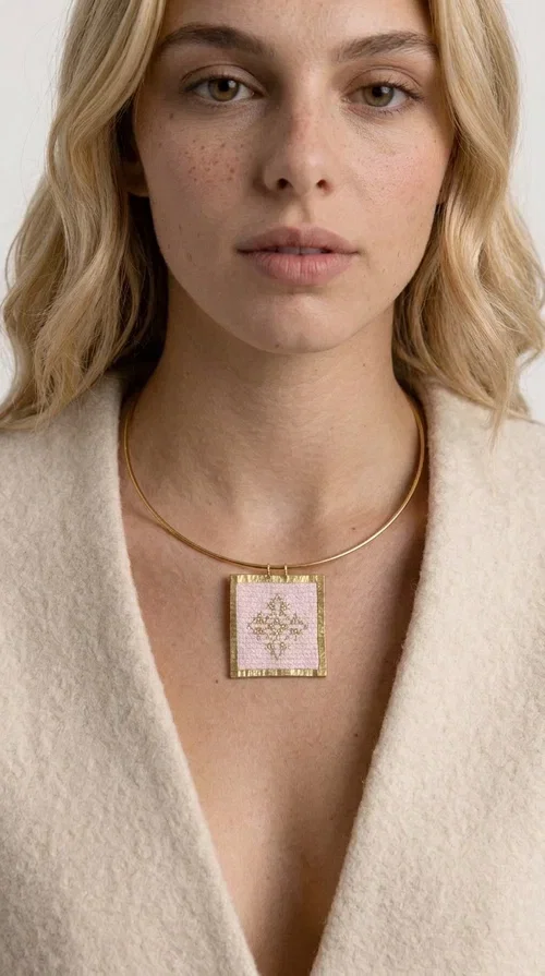 , An embroidered necklace that combines the traditional art of embroidery with modern design, creating a piece of jewelry that stands out instantly.

Designed by Greek Jewelry Designer Aikaterini Chalkiadaki, this statement necklace features a rectangular embroidered motif in soft pink tones with gold geometric details inspired by Greek folk tradition. The gold brass frame highlights the embroidered fabric, while the delicate semicircular chain gives the whole piece an airy and elegant character.

Ideal for women who love striking jewelry with soul, this handmade necklace pairs perfectly with both casual and more formal outfits — just as shown here over a classic beige jacket. Bring folk aesthetics into your everyday look in a completely modern way.