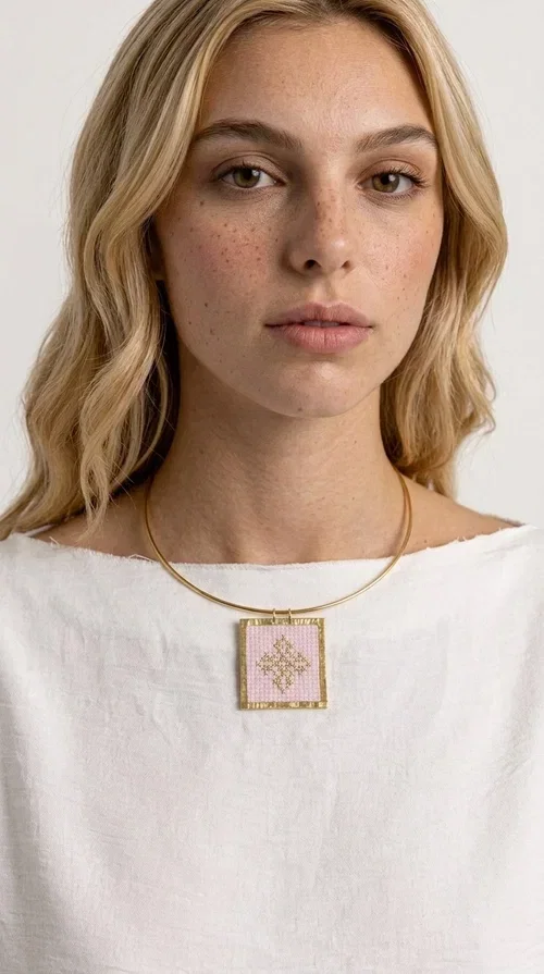 , An embroidered necklace that combines the traditional art of embroidery with modern design, creating a piece of jewelry that stands out instantly.

Designed by Greek Jewelry Designer Aikaterini Chalkiadaki, this statement necklace features a rectangular embroidered motif in soft pink tones with gold geometric details inspired by Greek folk tradition. The gold brass frame highlights the embroidered fabric, while the delicate semicircular chain gives the whole piece an airy and elegant character.

Ideal for women who love striking jewelry with soul, this handmade necklace pairs perfectly with both casual and more formal outfits — just as shown here over a classic beige jacket. Bring folk aesthetics into your everyday look in a completely modern way.