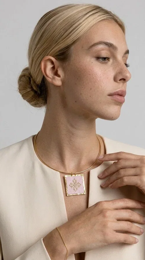, An embroidered necklace that combines the traditional art of embroidery with modern design, creating a piece of jewelry that stands out instantly.

Designed by Greek Jewelry Designer Aikaterini Chalkiadaki, this statement necklace features a rectangular embroidered motif in soft pink tones with gold geometric details inspired by Greek folk tradition. The gold brass frame highlights the embroidered fabric, while the delicate semicircular chain gives the whole piece an airy and elegant character.

Ideal for women who love striking jewelry with soul, this handmade necklace pairs perfectly with both casual and more formal outfits — just as shown here over a classic beige jacket. Bring folk aesthetics into your everyday look in a completely modern way.