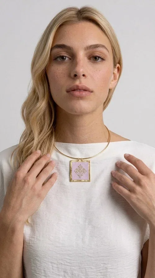 , An embroidered necklace that combines the traditional art of embroidery with modern design, creating a piece of jewelry that stands out instantly.

Designed by Greek Jewelry Designer Aikaterini Chalkiadaki, this statement necklace features a rectangular embroidered motif in soft pink tones with gold geometric details inspired by Greek folk tradition. The gold brass frame highlights the embroidered fabric, while the delicate semicircular chain gives the whole piece an airy and elegant character.

Ideal for women who love striking jewelry with soul, this handmade necklace pairs perfectly with both casual and more formal outfits — just as shown here over a classic beige jacket. Bring folk aesthetics into your everyday look in a completely modern way.