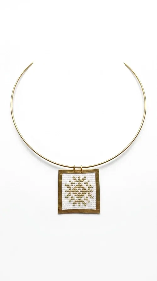 , An embroidered necklace that combines tradition with modern aesthetics — the Statement Necklace KOL-4721 is a handmade creation that stands out for its refined detail and unique character. Designed by Greek Jewelry Designer Aikaterini Chalkiadaki, this piece pays tribute to the folk Greek art of embroidery, rendering geometric motifs on white fabric with gold details.

The rectangular embroidered pendant, featuring a handcrafted gold-tone brass frame, hangs from a classic gold omega-style necklace chain, which adds stability and elegance to the overall look. The folklore geometric patterns on the white fabric create an eye-catching contrast, while the overall aesthetic moves between ethnic and contemporary style.

Ideal for pairing with linen or wool clothing in neutral tones, it suits both casual and more formal looks. A true statement piece for the neck that needs no other additions to shine.