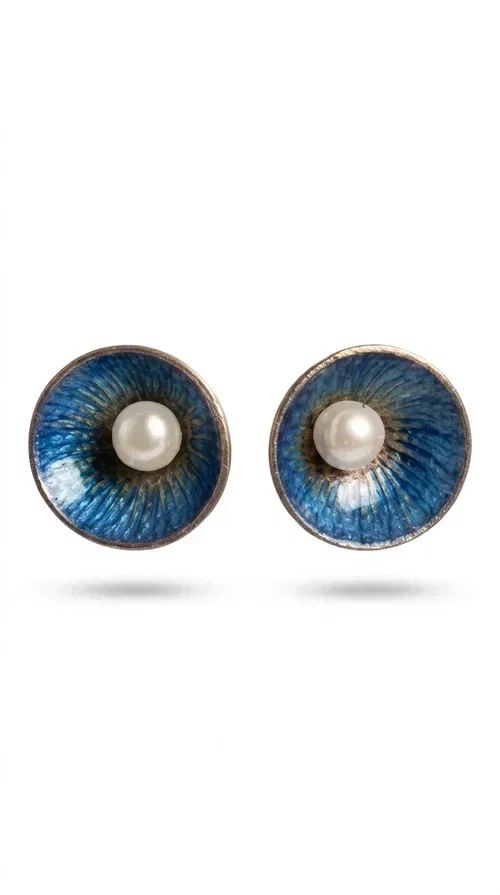 , The handmade stud earrings with a pearl in deep blue enamel are an ideal choice for every woman seeking elegance with character. Designed by Greek Jewelry Designer Aikaterini Chalkiadaki, these unique earrings combine the traditional technique of enamel with the timeless grace of the pearl, creating a result that impresses without being overwhelming.

The circular brass body is covered with handmade enamel in rich shades of blue — from deep navy to cobalt — with subtle color variations reminiscent of the ocean depths. At the center, a white pearl adds finesse and contrast, elevating the whole piece to another level. The result is a statement piece of jewelry that suits an everyday look just as well as a wedding or formal outfit.