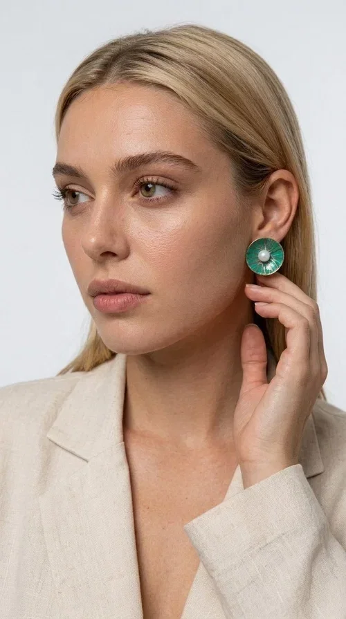 , Handmade stud earrings with pearls in deep green are a choice that combines elegance and character, ideal for every woman who loves accessories with personality. Designed by Greek Jewelry Designer Aikaterini Chalkiadaki, these earrings are a unique combination of handmade artistry and contemporary aesthetics.

Made of brass and enamel in a vivid green tone, these earrings feature a central pearl that adds a delicate, feminine touch to a bold design. Their round, disc-shaped form with a woven-textured enamel surface creates an interesting visual texture that catches the eye without being overwhelming. The result is a piece of jewelry that stands on its own — the perfect statement piece for both everyday and evening looks.

They pair equally beautifully with casual outfits, professional looks, and formal events such as weddings and christenings. The green color flatters every skin tone and blends harmoniously with neutral, white, and bold colors alike.