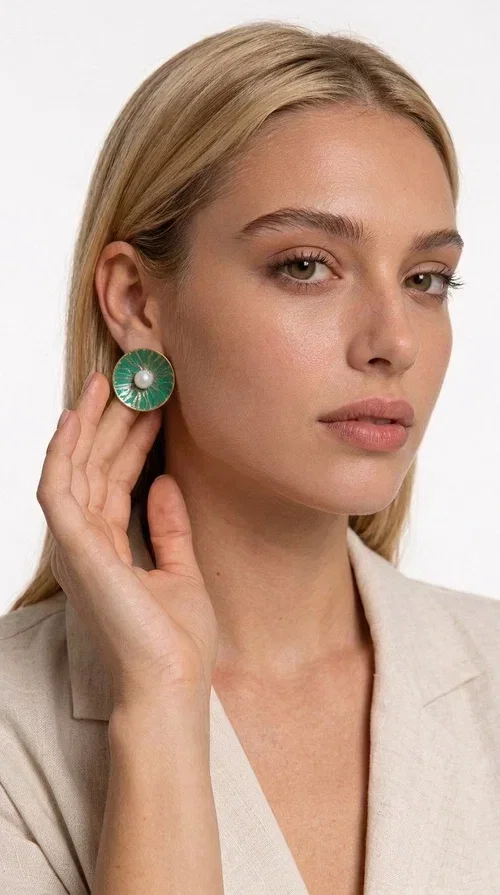 , Handmade stud earrings with pearls in deep green are a choice that combines elegance and character, ideal for every woman who loves accessories with personality. Designed by Greek Jewelry Designer Aikaterini Chalkiadaki, these earrings are a unique combination of handmade artistry and contemporary aesthetics.

Made of brass and enamel in a vivid green tone, these earrings feature a central pearl that adds a delicate, feminine touch to a bold design. Their round, disc-shaped form with a woven-textured enamel surface creates an interesting visual texture that catches the eye without being overwhelming. The result is a piece of jewelry that stands on its own — the perfect statement piece for both everyday and evening looks.

They pair equally beautifully with casual outfits, professional looks, and formal events such as weddings and christenings. The green color flatters every skin tone and blends harmoniously with neutral, white, and bold colors alike.