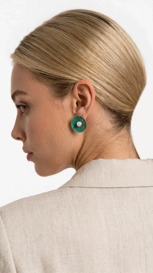 , Handmade stud earrings with pearls in deep green are a choice that combines elegance and character, ideal for every woman who loves accessories with personality. Designed by Greek Jewelry Designer Aikaterini Chalkiadaki, these earrings are a unique combination of handmade artistry and contemporary aesthetics.

Made of brass and enamel in a vivid green tone, these earrings feature a central pearl that adds a delicate, feminine touch to a bold design. Their round, disc-shaped form with a woven-textured enamel surface creates an interesting visual texture that catches the eye without being overwhelming. The result is a piece of jewelry that stands on its own — the perfect statement piece for both everyday and evening looks.

They pair equally beautifully with casual outfits, professional looks, and formal events such as weddings and christenings. The green color flatters every skin tone and blends harmoniously with neutral, white, and bold colors alike.