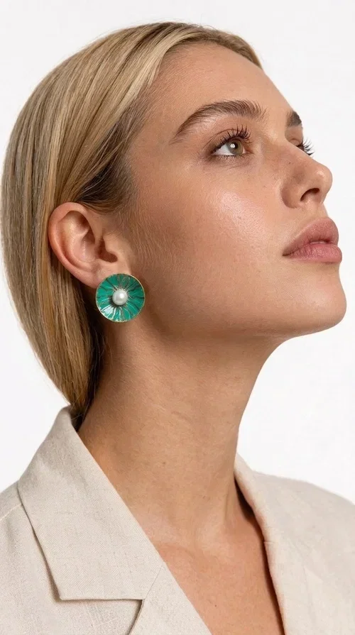 , Handmade stud earrings with pearls in deep green are a choice that combines elegance and character, ideal for every woman who loves accessories with personality. Designed by Greek Jewelry Designer Aikaterini Chalkiadaki, these earrings are a unique combination of handmade artistry and contemporary aesthetics.

Made of brass and enamel in a vivid green tone, these earrings feature a central pearl that adds a delicate, feminine touch to a bold design. Their round, disc-shaped form with a woven-textured enamel surface creates an interesting visual texture that catches the eye without being overwhelming. The result is a piece of jewelry that stands on its own — the perfect statement piece for both everyday and evening looks.

They pair equally beautifully with casual outfits, professional looks, and formal events such as weddings and christenings. The green color flatters every skin tone and blends harmoniously with neutral, white, and bold colors alike.