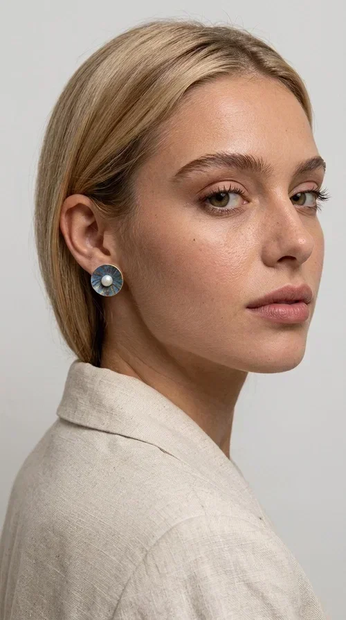 , These handmade stud earrings with pearls in deep blue color are an elegant choice for every woman seeking jewelry with character and quality. Designed by Greek Jewelry Designer Aikaterini Chalkiadaki, these earrings combine the traditional art of enamel with the timeless beauty of the pearl, creating a result that truly stands out.

The circular brass shape with a relief surface in a radiant sunburst pattern gives the piece an open, flower-like character. The blue-toned enamel evenly covers the base, while at the center a white pearl stands out, adding finesse and contrast. Their stud design makes them ideal for everyday wear, as well as for formal occasions.

Wear them paired with linen or neutral outfits to highlight their color palette, or choose them as a statement piece for weddings, christenings, and every special moment.